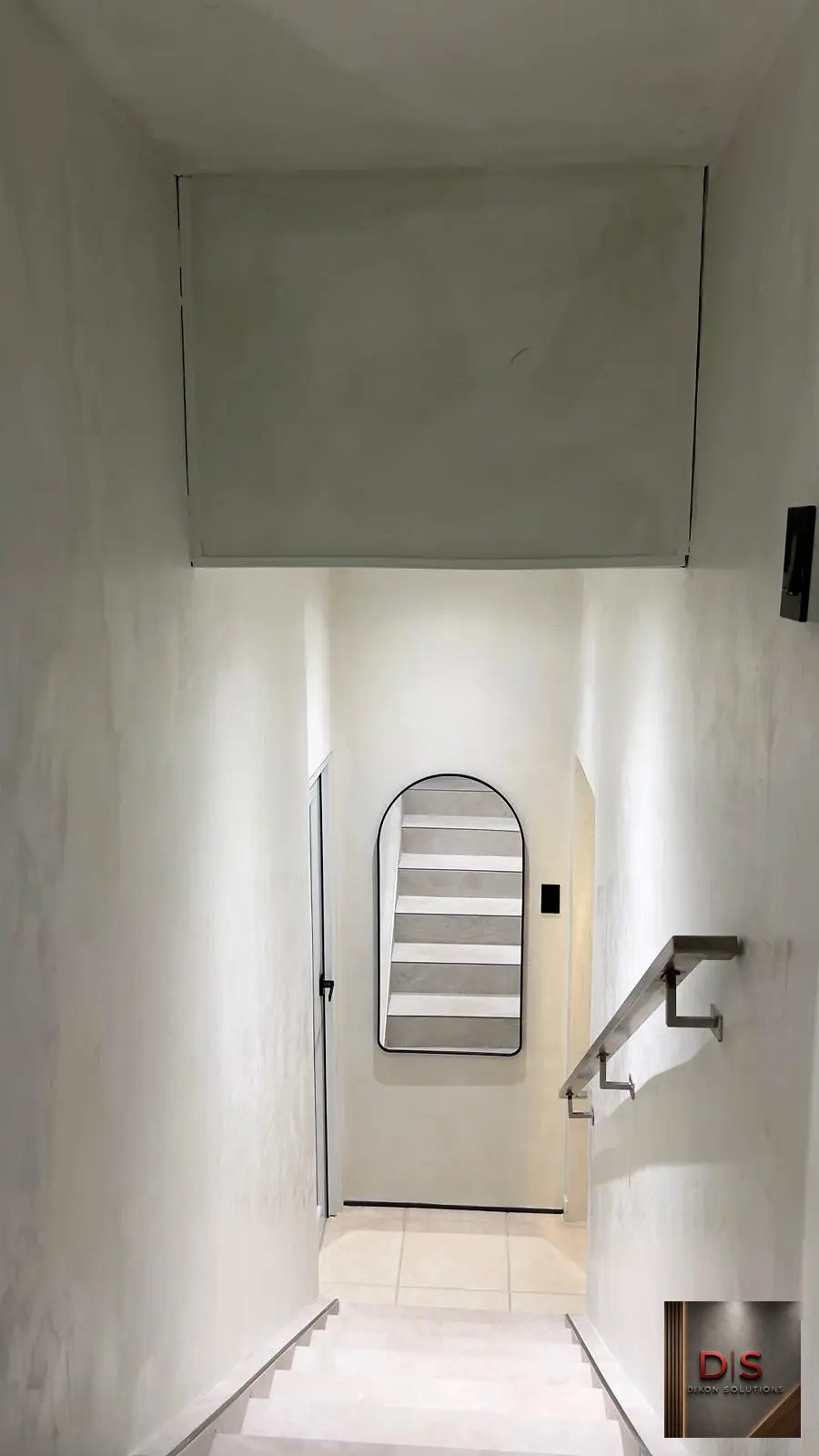Escalera interior con paredes claras de cemento pulido y espejo arqueado